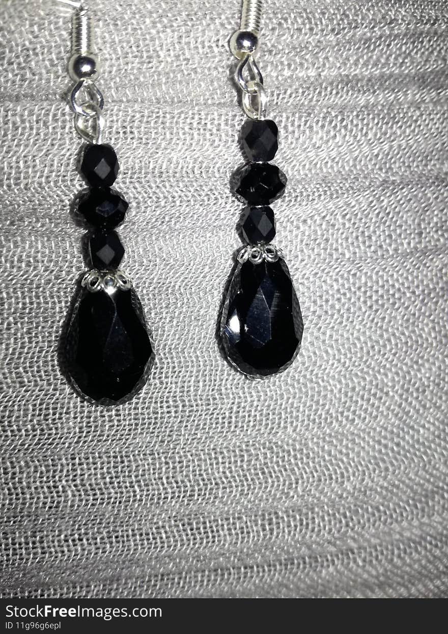 On a nice textile background texture, a photo of some beautiful black semiprecious stone with sterling silver accessories earrings, made by my mom of course. On a nice textile background texture, a photo of some beautiful black semiprecious stone with sterling silver accessories earrings, made by my mom of course