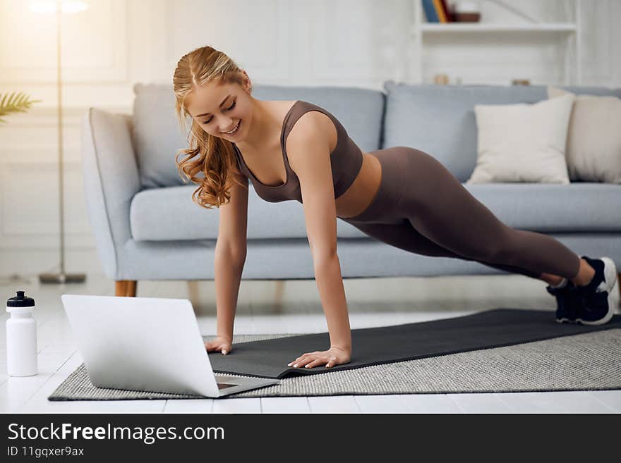Fit young woman wearing sportswear working out at home doing planking exercise on carpet