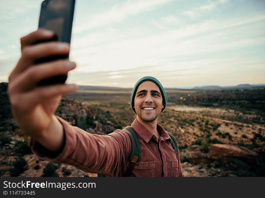 Caucasian male photographer hiking in wilderness taking images and selfies on cellular device embracing outdoors. High quality photo