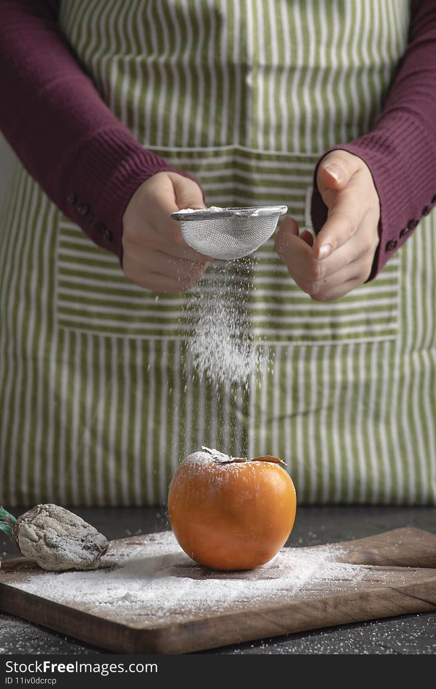 Female cook spilling flour to sweet persimmon in kitchen. High quality photo