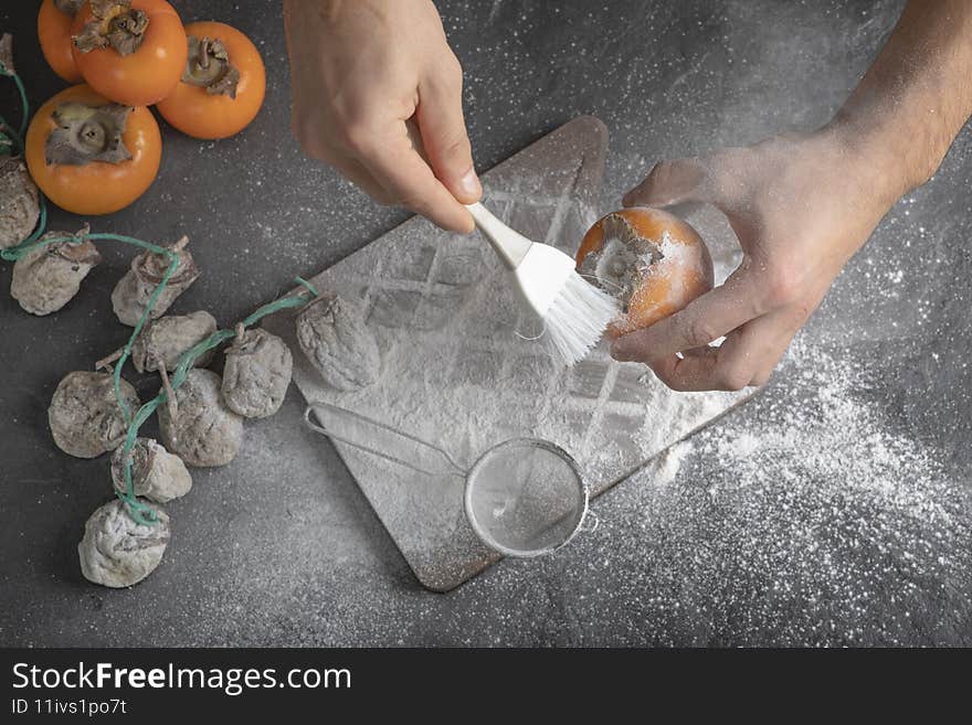 Female cook decorating persimmon with flour on black background