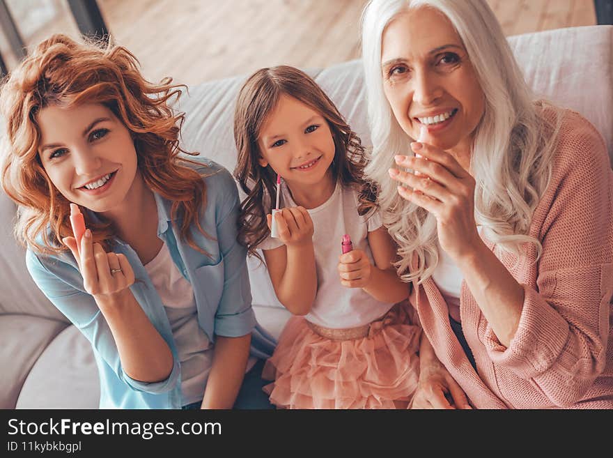 Portrait of grandmother, mother and daughter applying lips with lipsticks.