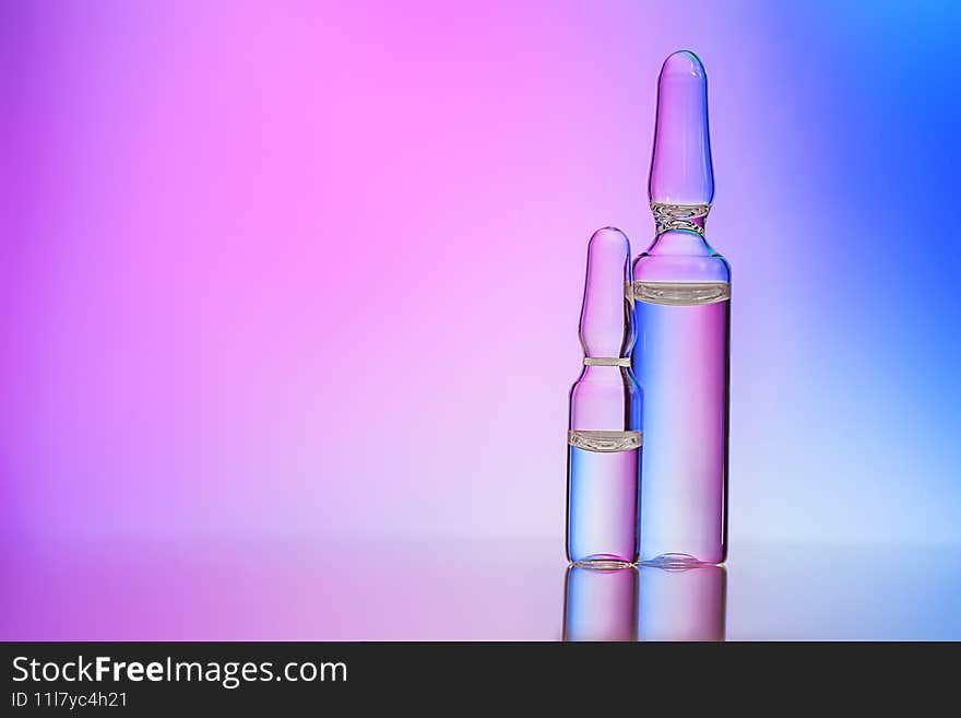 Two glass medical ampoules with clear liquid over colorful background. Medicine, vactination, Injection, drug concept