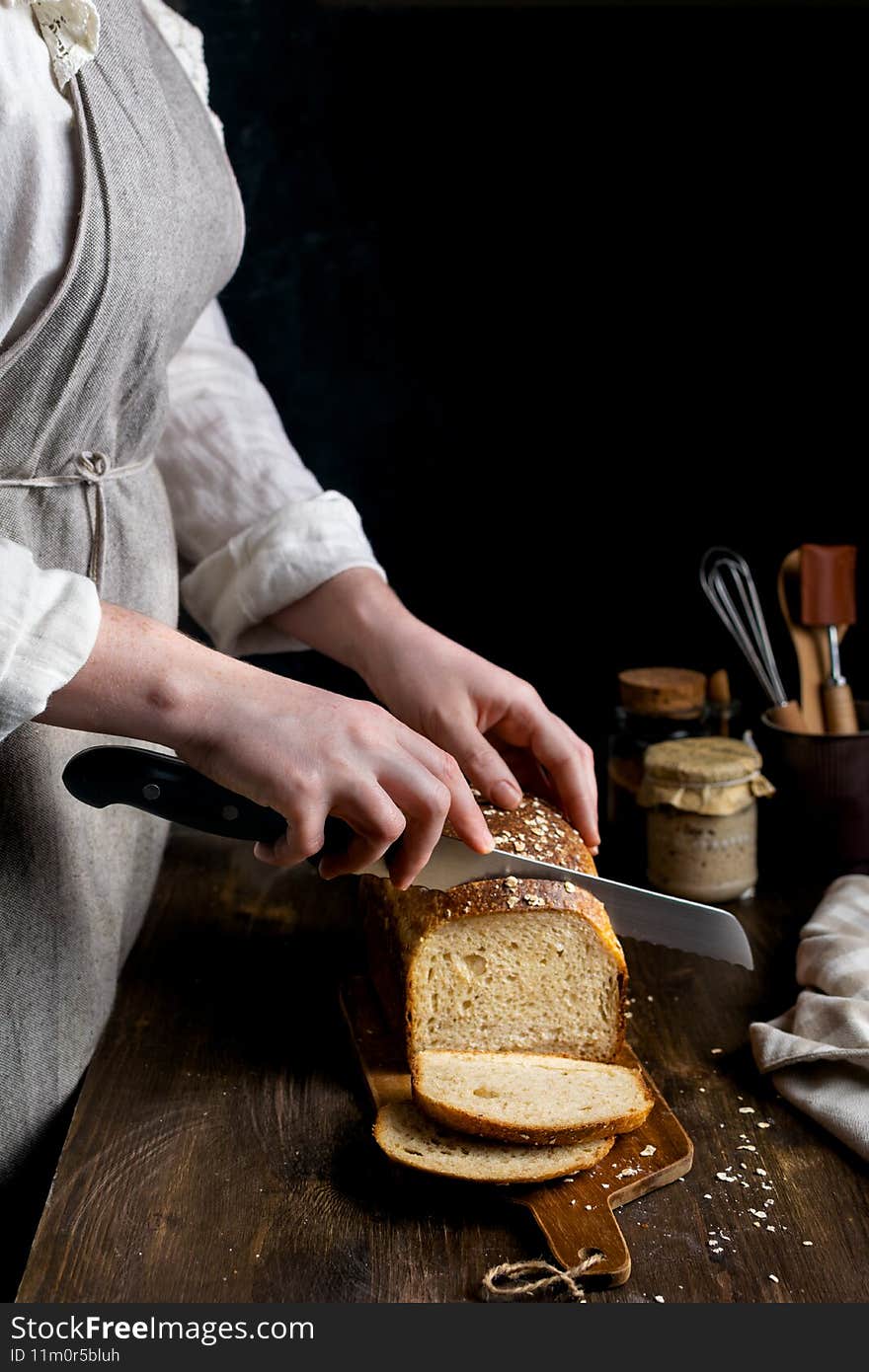 Close up of female hands cutting homemade whole grain sourdough bread on dark background, copy space. Close up of female hands cutting homemade whole grain sourdough bread on dark background, copy space