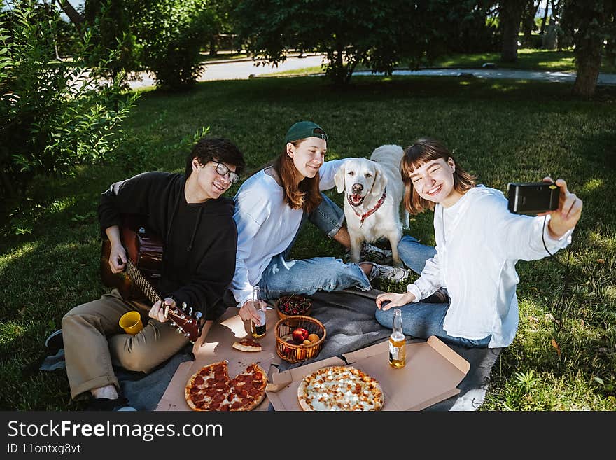 Company of beautiful young people and dog having an outdoor lunch.