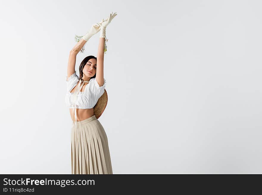 brunette woman in stylish spring outfit and gloves with flowers posing with hands above head  on white,stock image