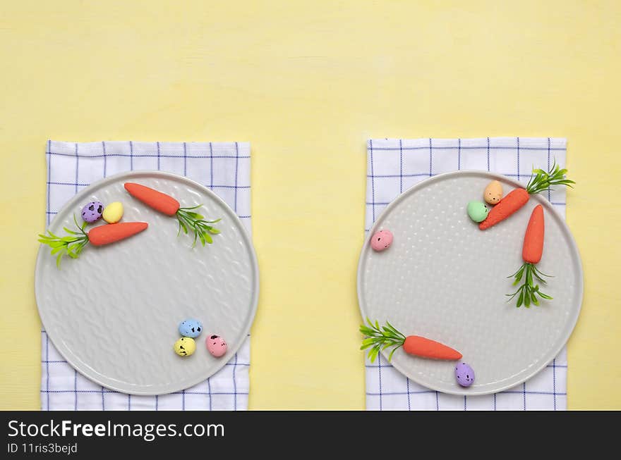 Top view of grey plates, napkins and nest, decorative eggs and carrots on the yellow table.Empty space.Easter concept