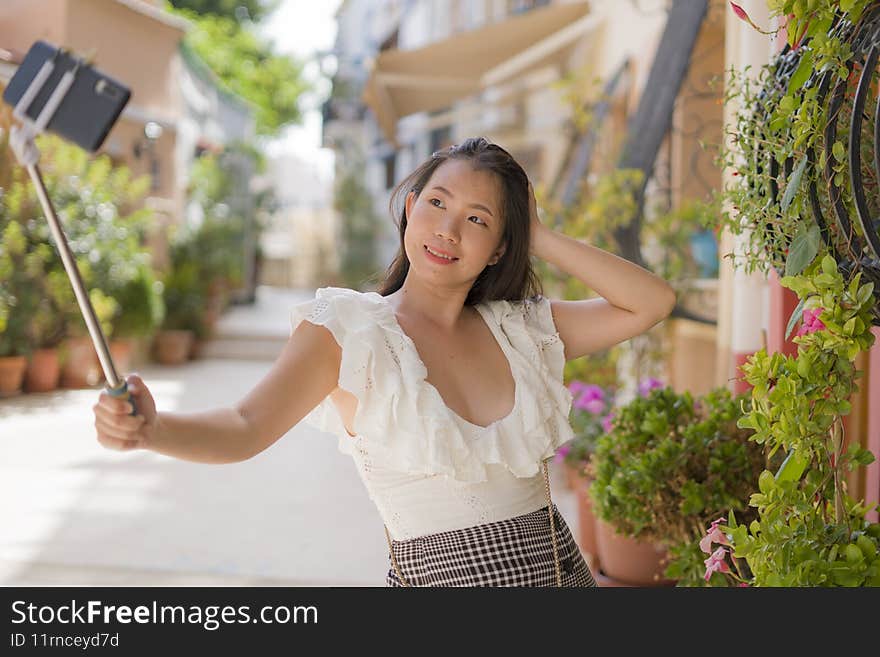 Asian woman taking selfie as tourist in Andalusia Spain - young happy and beautiful Japanese girl taking self portrait with mobile