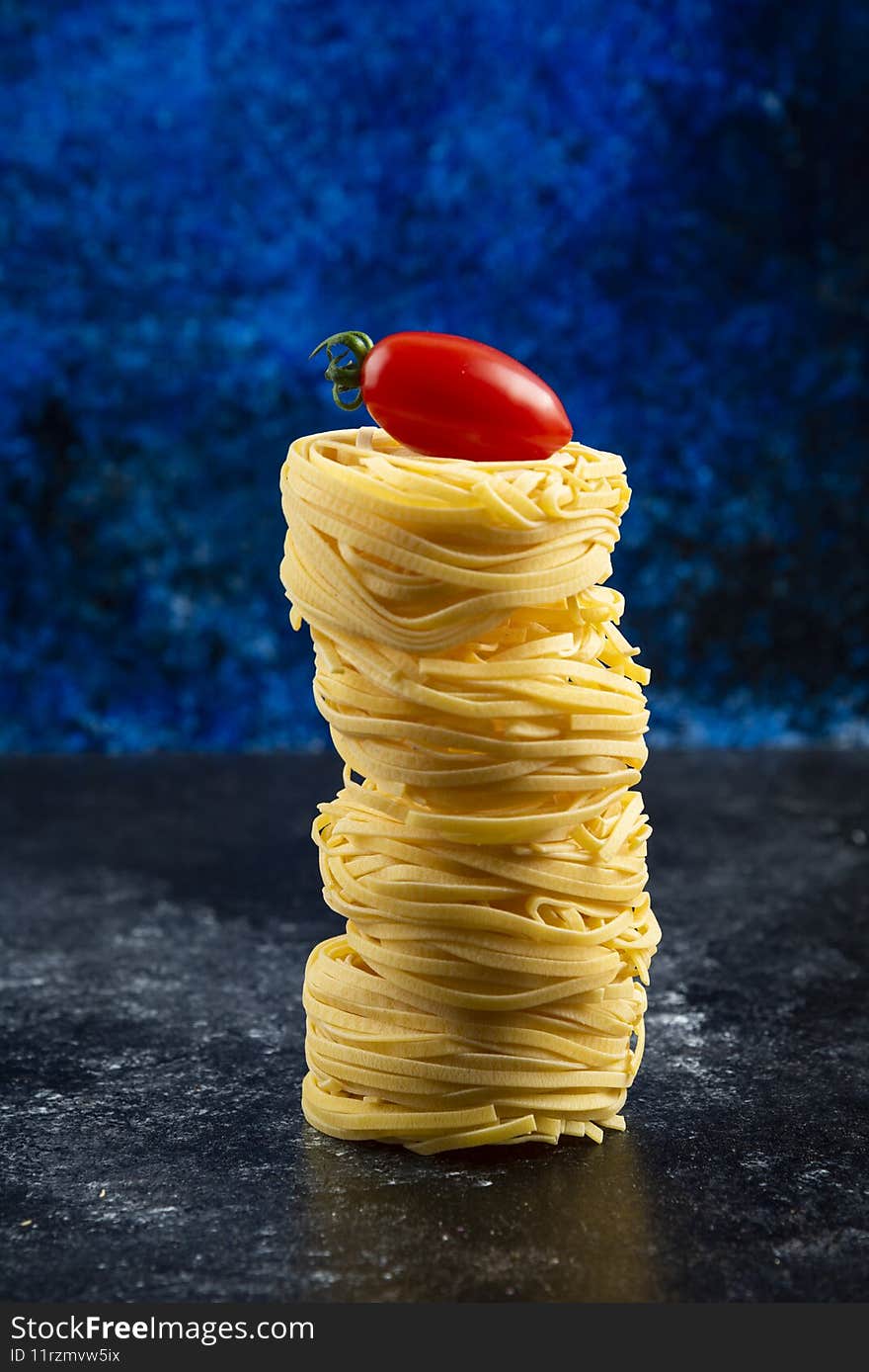 Uncooked pasta nests and tomato on marble table. High quality photo