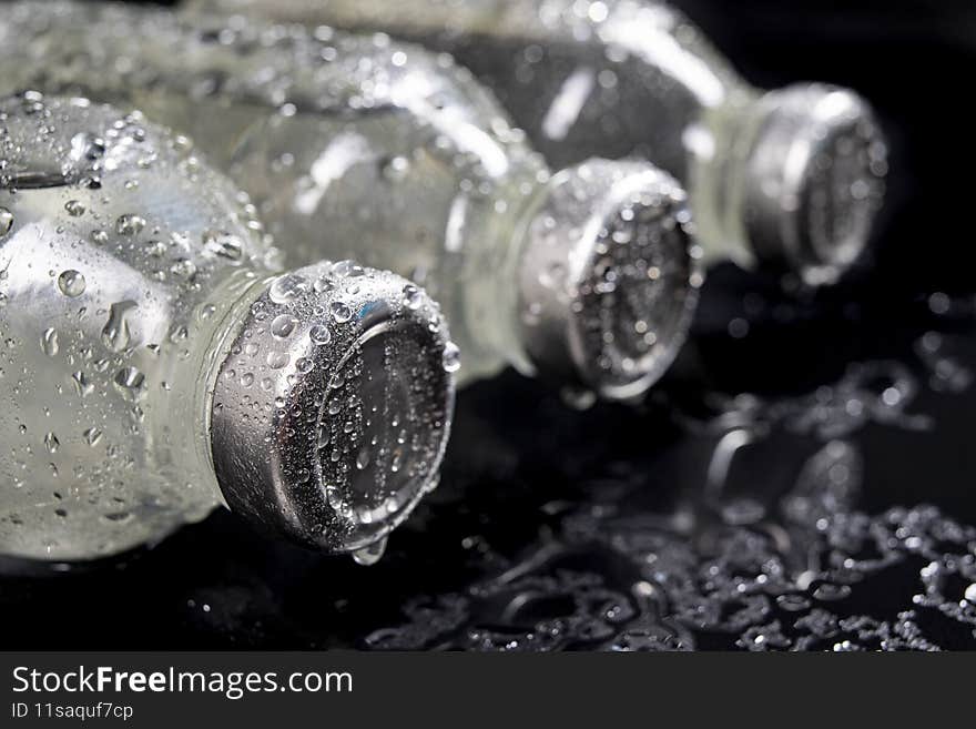 Glass bottles with fresh drinking water. Water drops on glass containers for water storage. Dark background