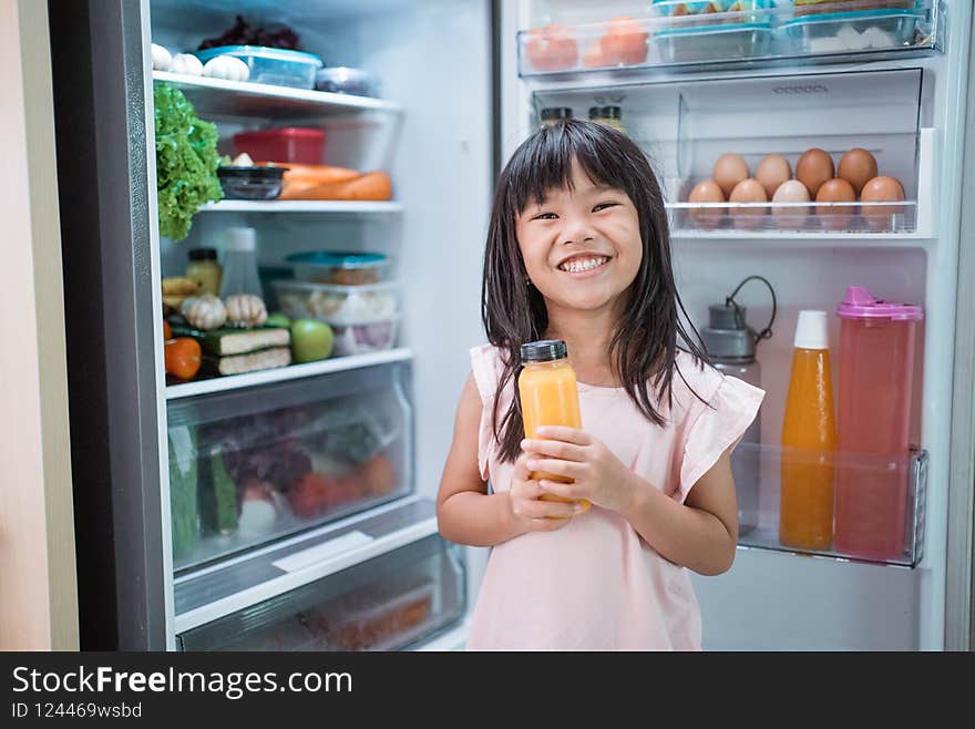 happy young asian girl open fridge door drinking a bottle of juice