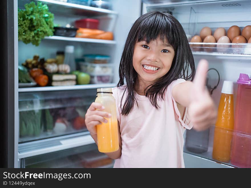 happy young asian girl open fridge door drinking a bottle of juice