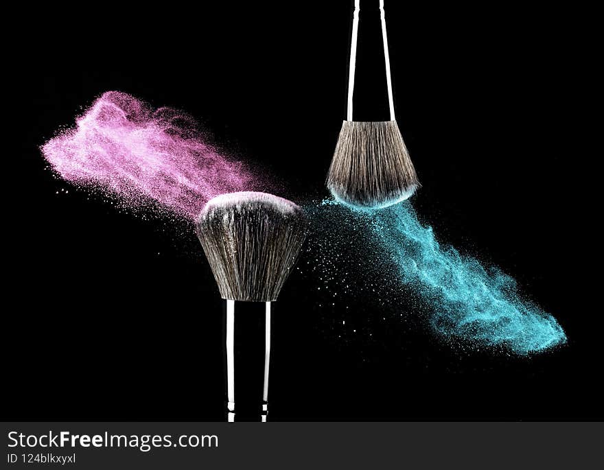 Makeup brushes with blue and purple powder explosion on black background. Makeup brushes with blue and purple powder explosion on black background.