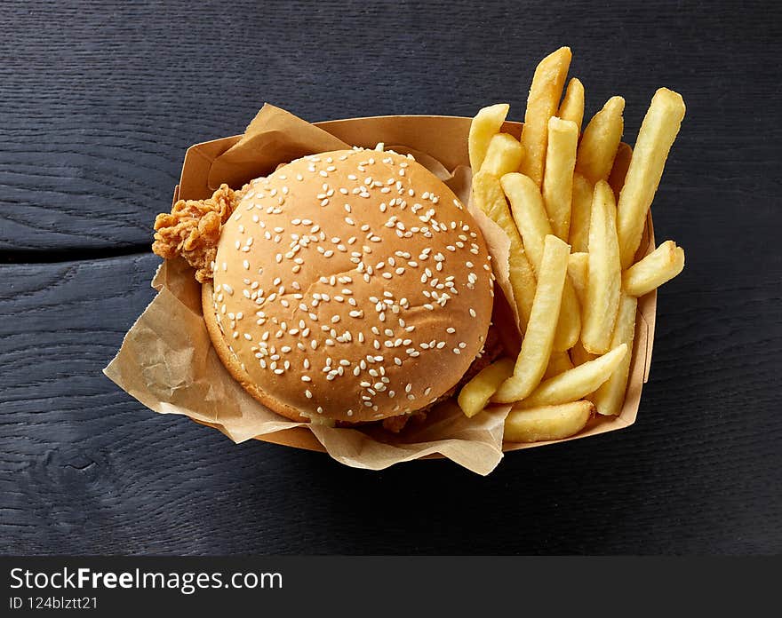 Fresh tasty burger and fried potatoes on black wooden table, top view