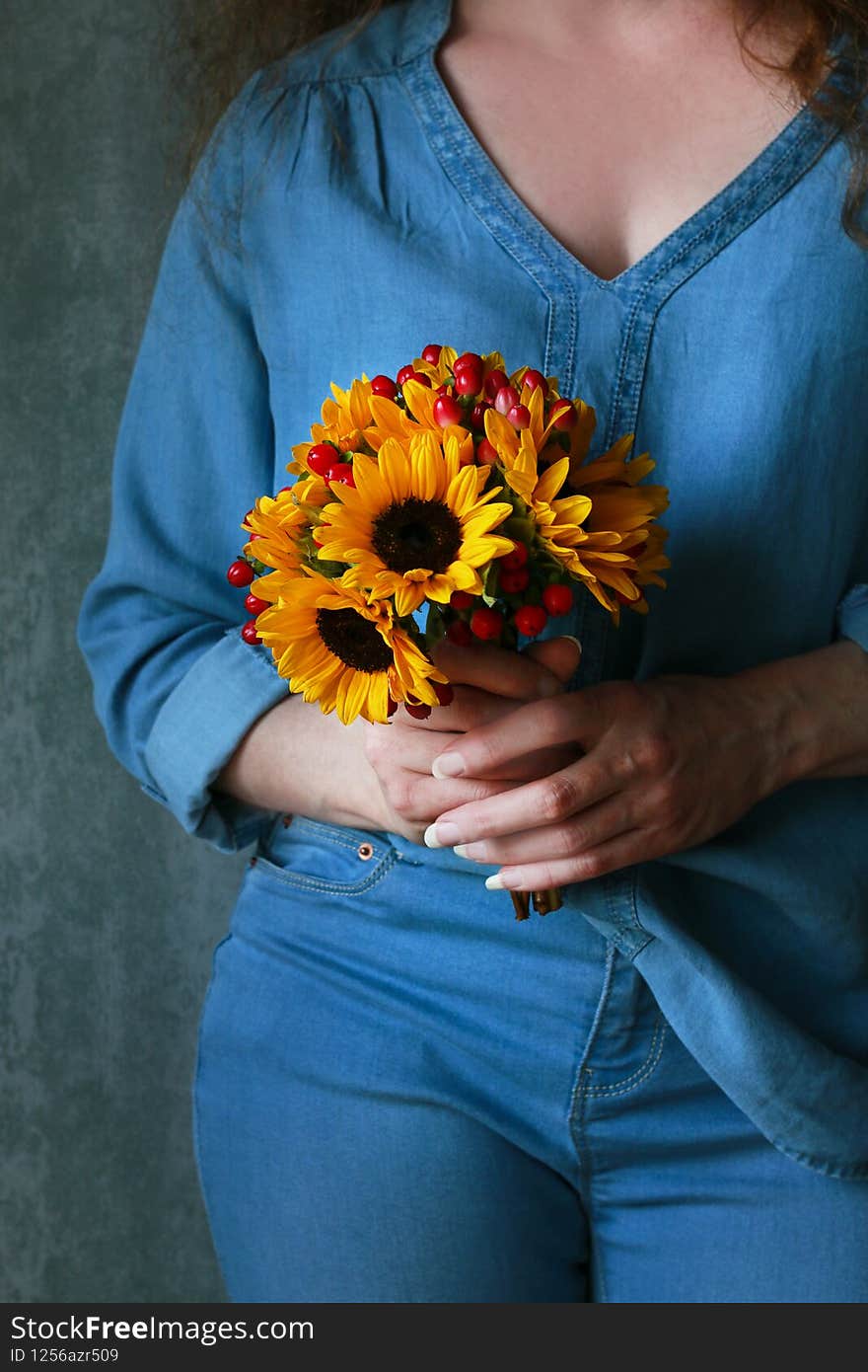 Woman in blue blouse holding bouquet of sunflowers and hypericum berries. Graphic resources