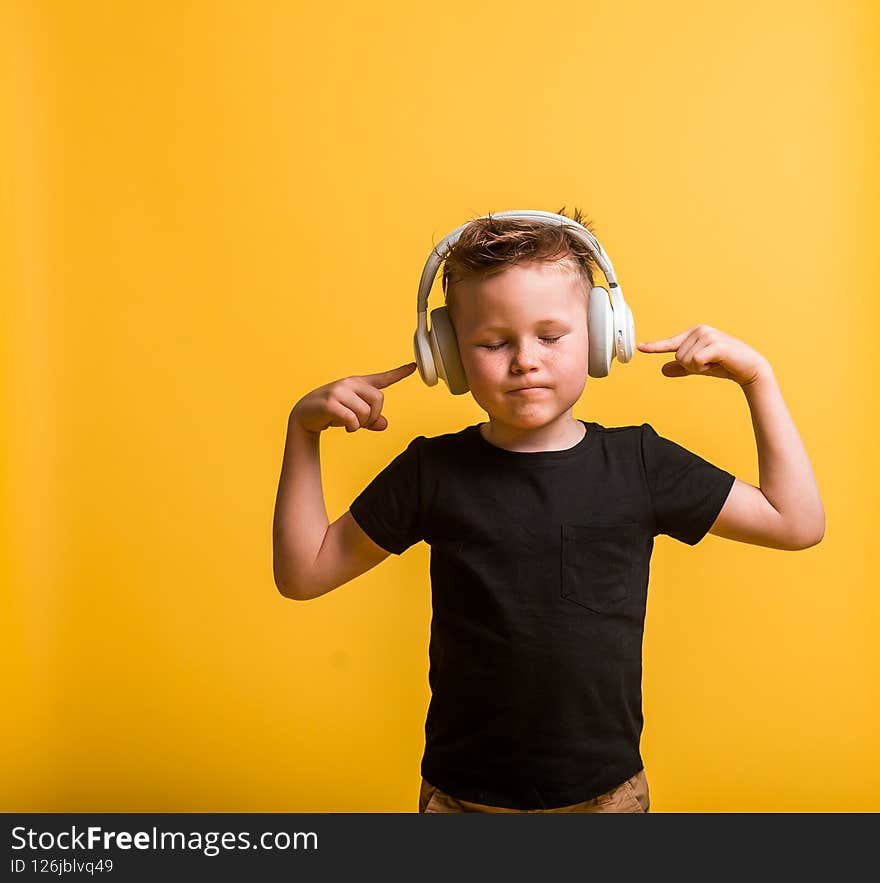Technology and music concept. little kid boy with headphones listening to music against yellow background at home. Stylish kid boy.