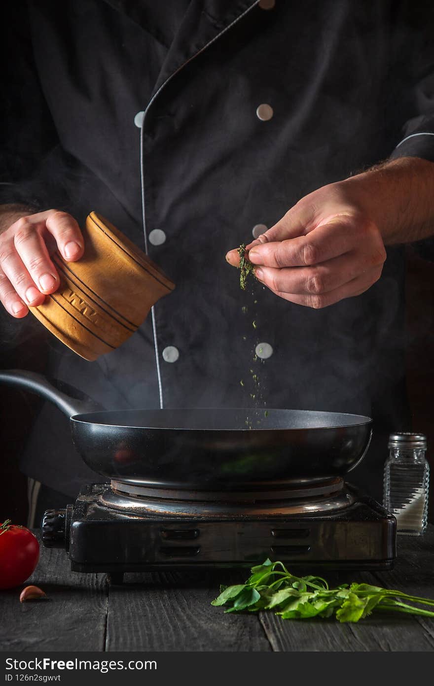 Professional chef pours spices into pan. Frozen motion. Concept cooking process in the restaurant kitchen. Vertical image