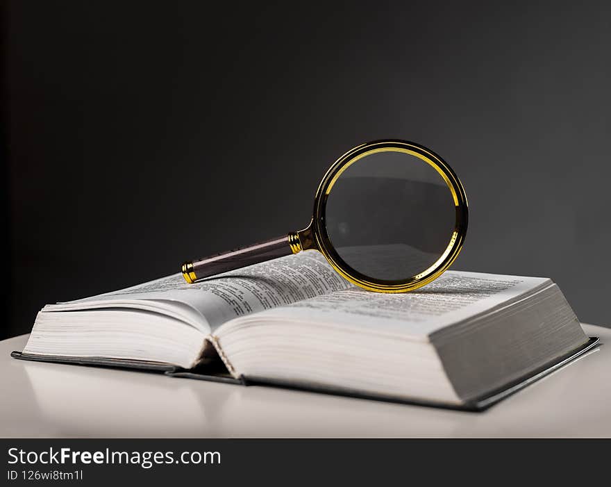 Open book closeup with turning pages and magnifying loupe. Textbook in hard cover on table. Studying and research concept.