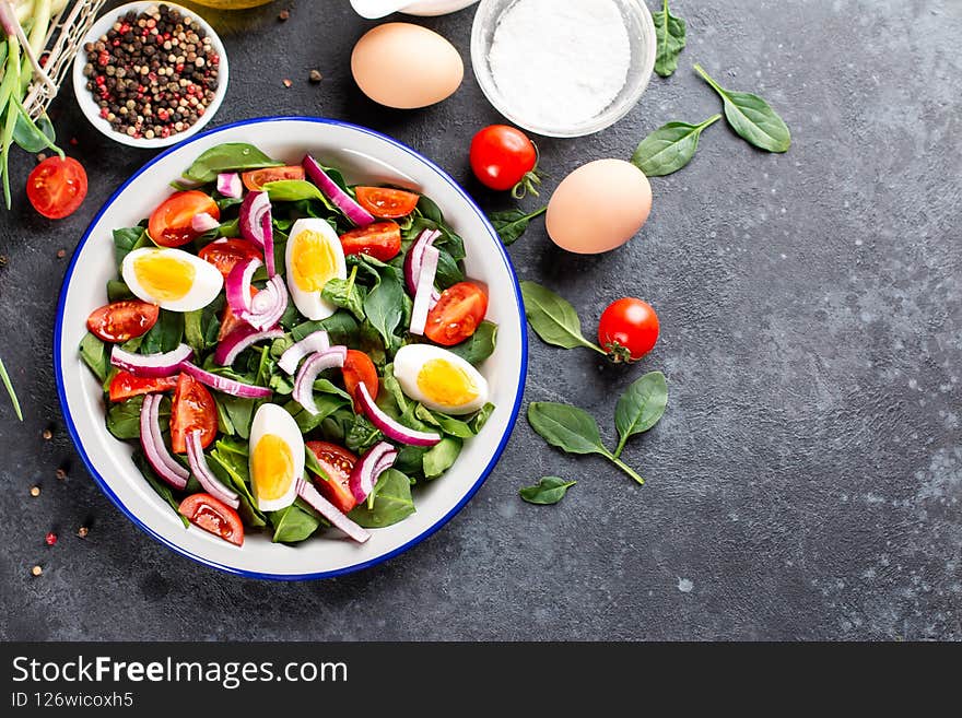 Salad with spinach leaves and eggs in bowl on a dark slate, stone or concrete background. Top view. Copy space