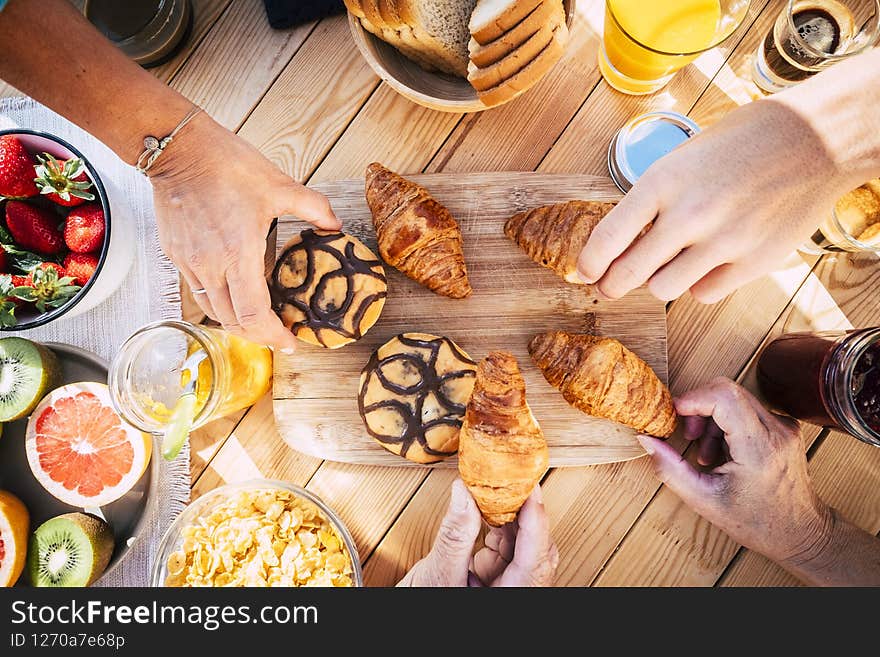 Top view of table with breakfast food and people eating together in friendship - family morning time and fresh bakery croissant - close up of hands picking brioches