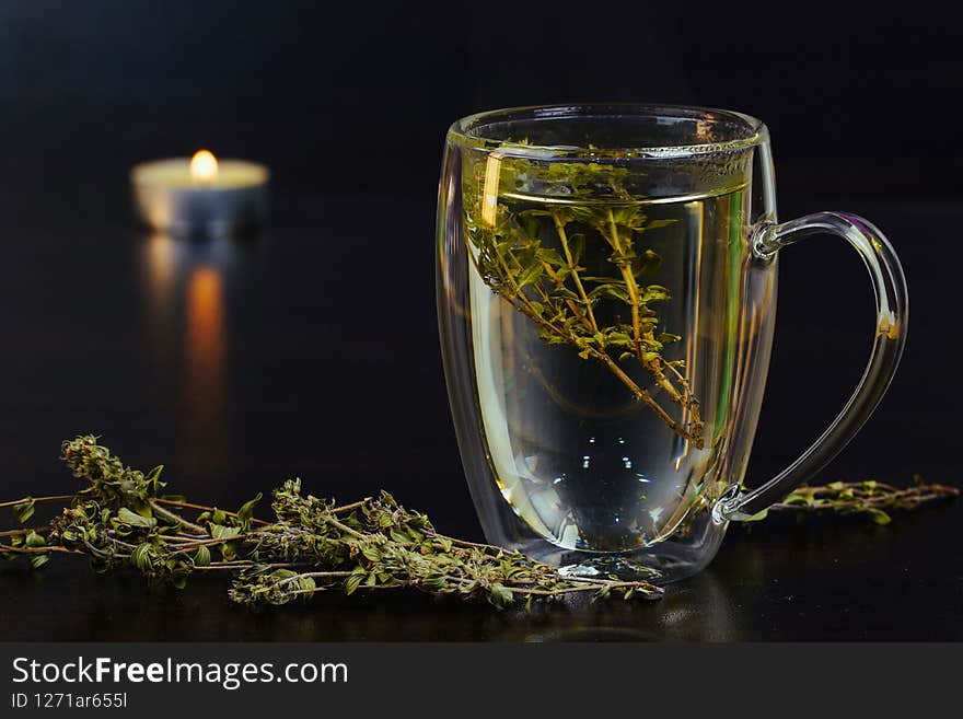 Burning candle on black background. Herbal Tea romantic design. Copy space. Tea production. Advertising image. Organic, herbal, natural, antibacterial tea in transparent cup,. Burning candle on black background. Herbal Tea romantic design. Copy space. Tea production. Advertising image. Organic, herbal, natural, antibacterial tea in transparent cup,