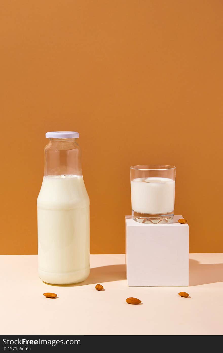 Glass with vegan milk from almond nuts with a bottle on white wooden tray with sunlit background. Dairy and lactose free substitute drink. Healthy food ingredient concept. Trendy colors. Glass with vegan milk from almond nuts with a bottle on white wooden tray with sunlit background. Dairy and lactose free substitute drink. Healthy food ingredient concept. Trendy colors
