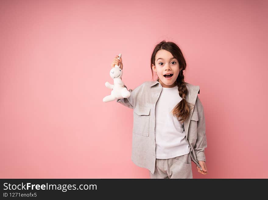 Beautiful girl in a sweater and a T-shirt rejoices at a gift to a toy hare standing on a pink background. High quality photo