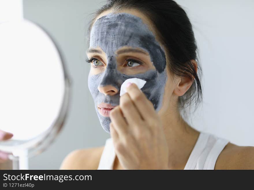 Woman washing off black clay mask from her face
