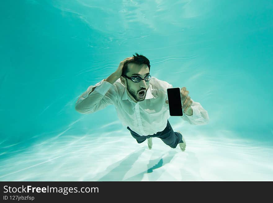 Amazed arabian businessman holding smartphone with blank screen underwater,stock image