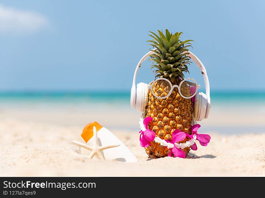 Summer in the party.  Hipster Pineapple Fashion in sunglass and listen music with sunblock and sandal on the sand beach beautiful blue sky background.  Creative art fruit for tropical style.   Fashion Summer Vacation Concept