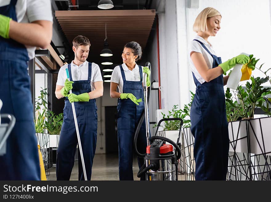 African american worker of cleaning company with vacuum cleaner talking to colleague in office,stock image