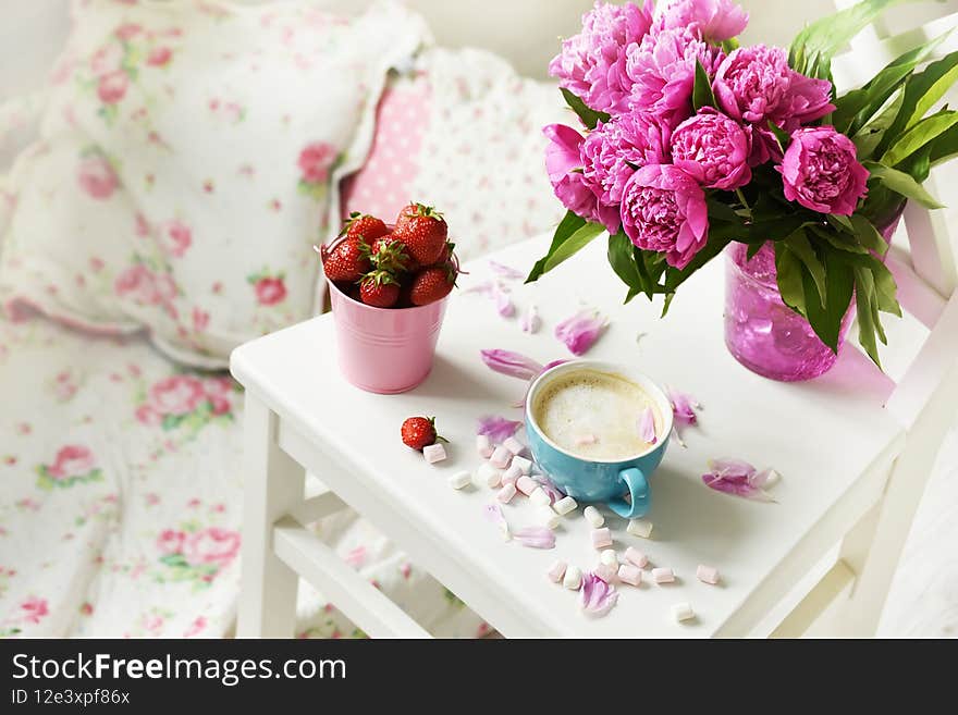 A bouquet of pink peonies and coffee with milk on a table in a bright room in the Provence style.