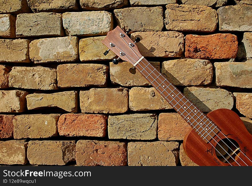 Photography of ukulele with brick wall in the background