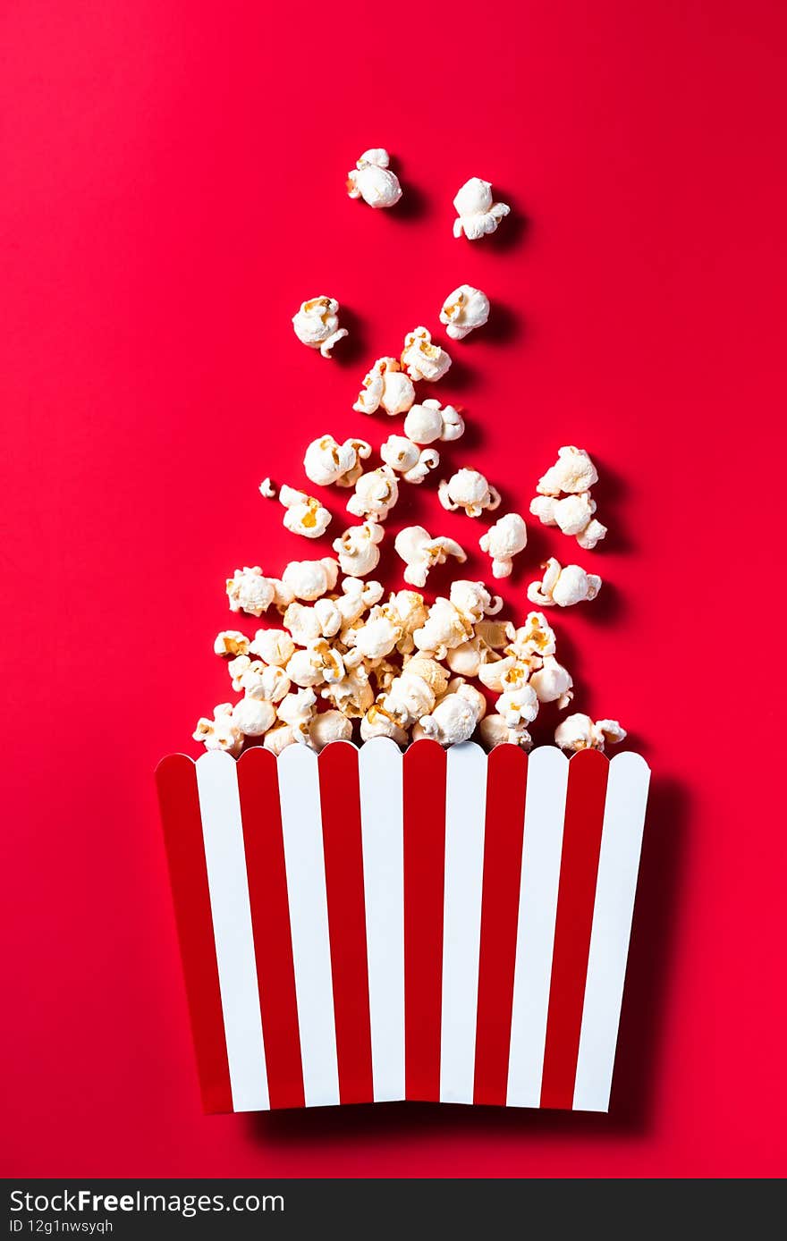 Striped Popcorn Bucket Box on Red Cinemab Background. Movies and Entertainment Concept. Flat Lay