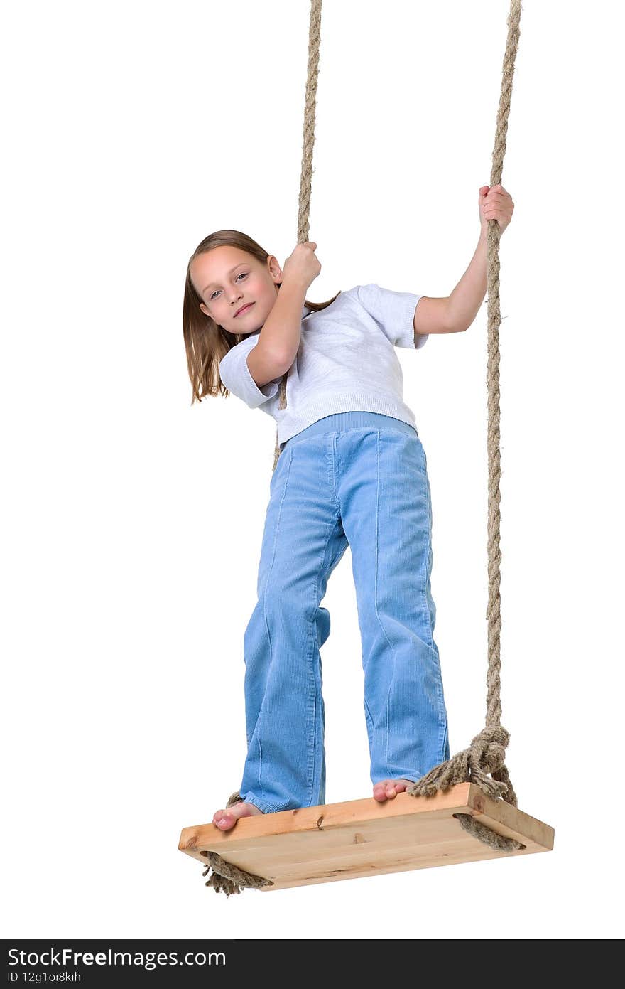 Preteen girl having fun on rope swing. Happy pretty barefoot girl dressed casual clothes standing on swing. Full length shot of preteen child swinging on isolated on white background