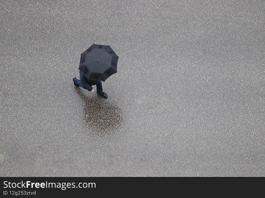 Rain in a city, lonely man with black umbrella crossing wet road, top view