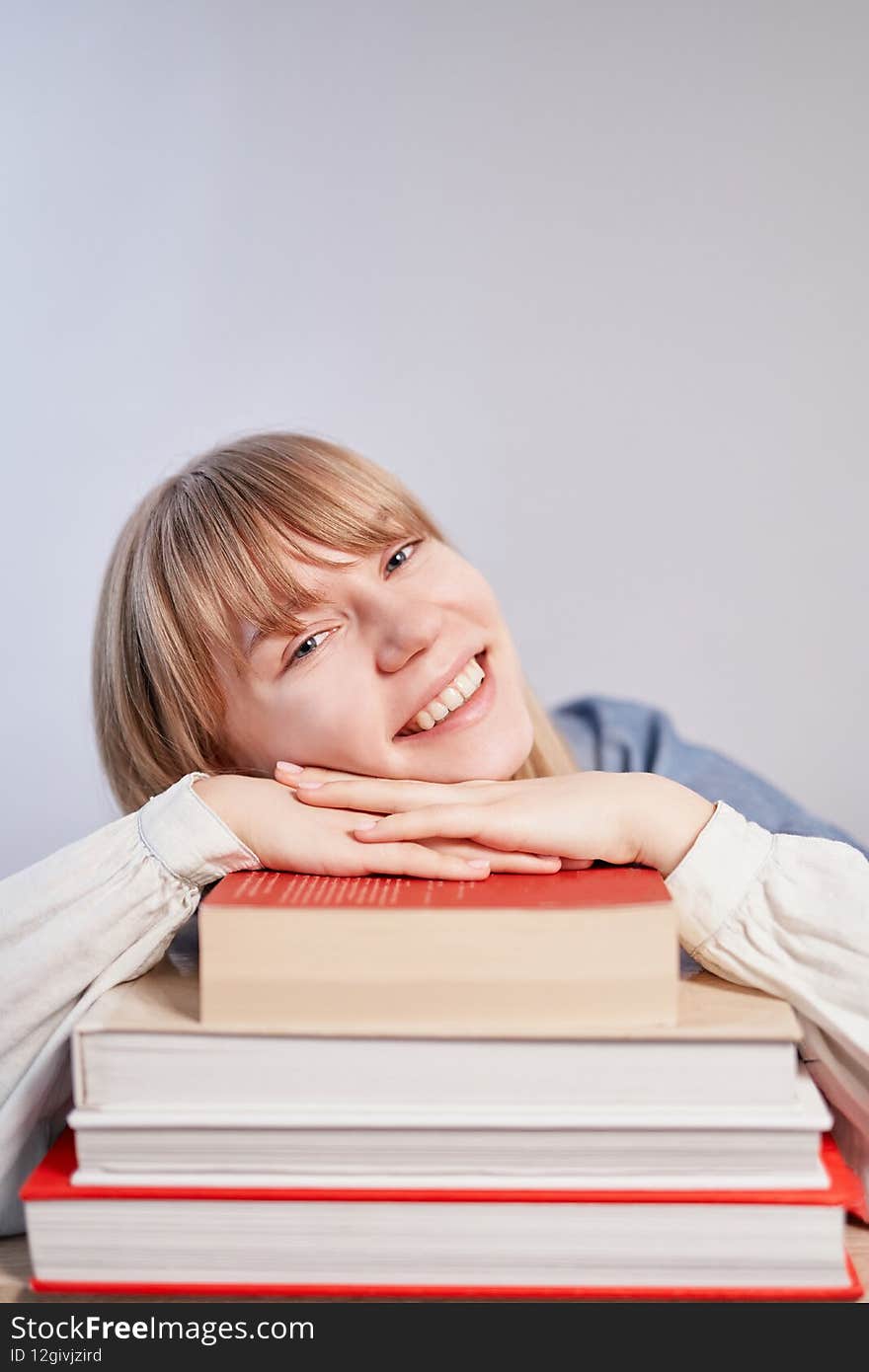 Caucasian blonde student girl relaxing lying on stack of books and smiling. Young female pupil with books in class with copy space. Back to school or homeschooling concept. High quality vertical photo. Caucasian blonde student girl relaxing lying on stack of books and smiling. Young female pupil with books in class with copy space. Back to school or homeschooling concept. High quality vertical photo