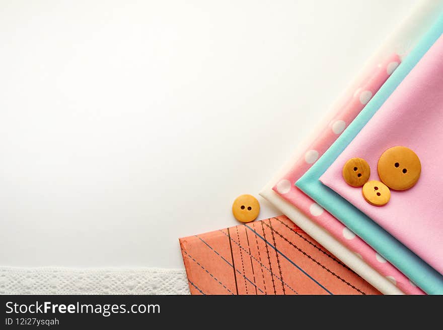 Cotton fabric of different colors, patterns and colored ribbons and wooden buttons on a white background. Space for text, top view.