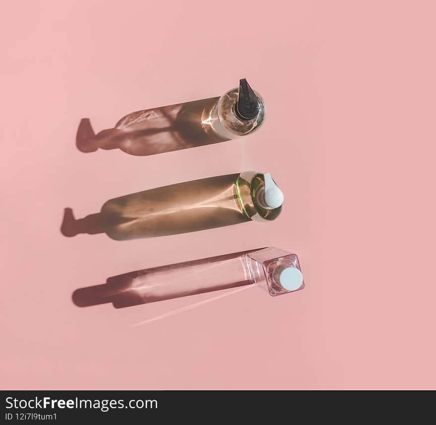 Three cosmetic product bottles in sunlight with shadow on pink background. Top view