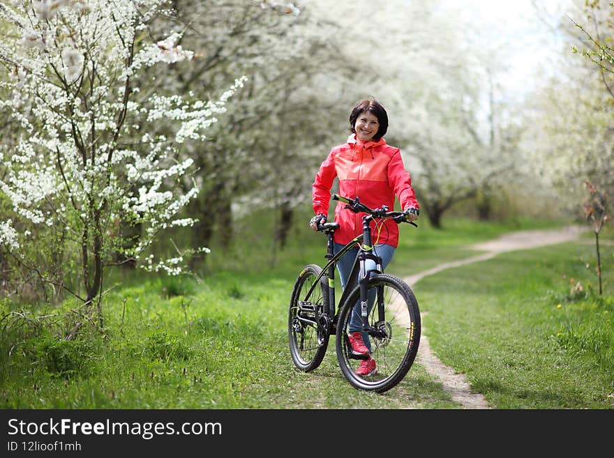 Beautiful woman on a bike in a blooming spring garden. Beautiful mature woman posing for the camera in a blooming spring garden.