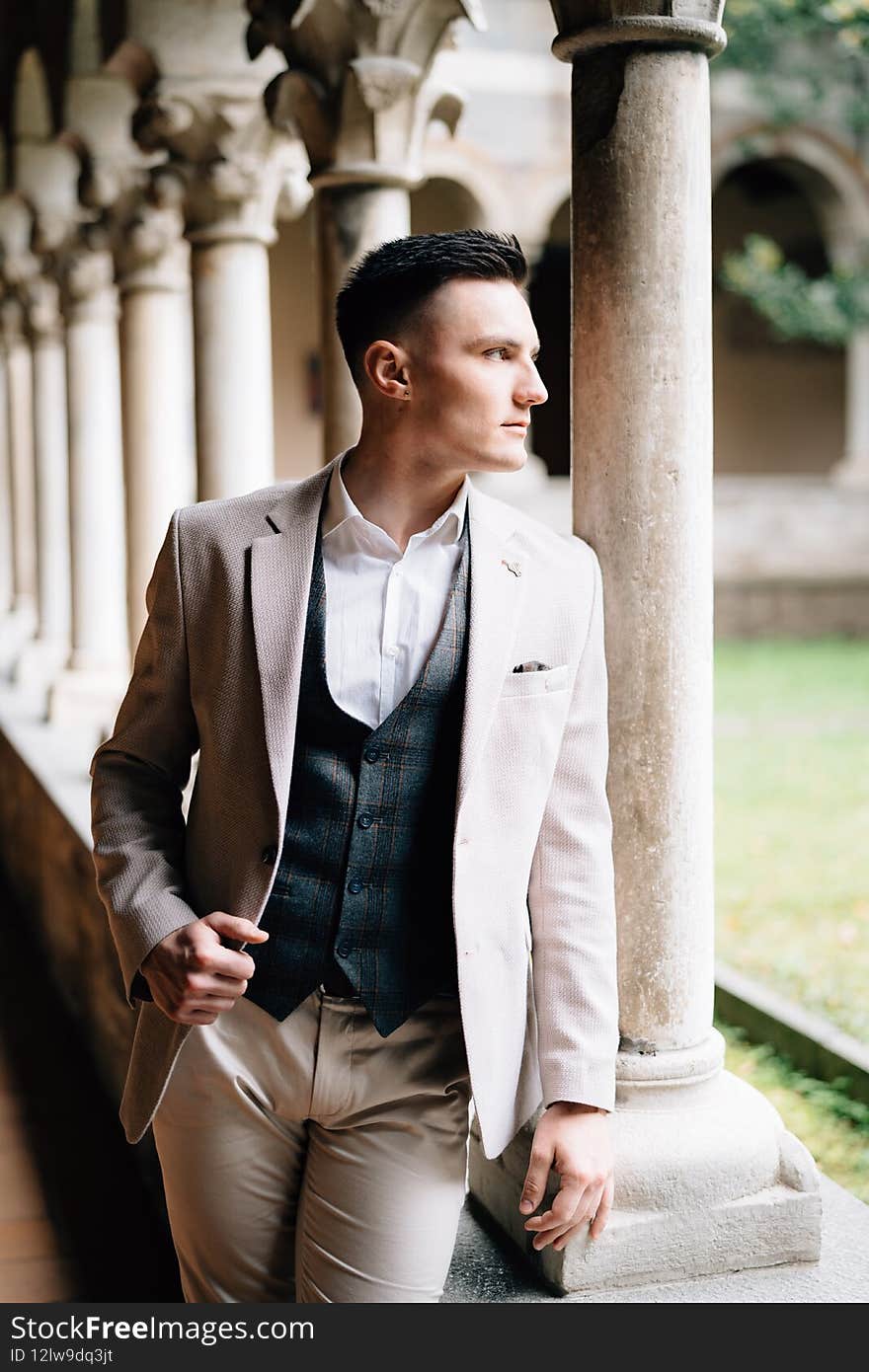 Groom in a suit stands leaning on the windowsill of a loggia with columns in an old building on Lake Como. Close up