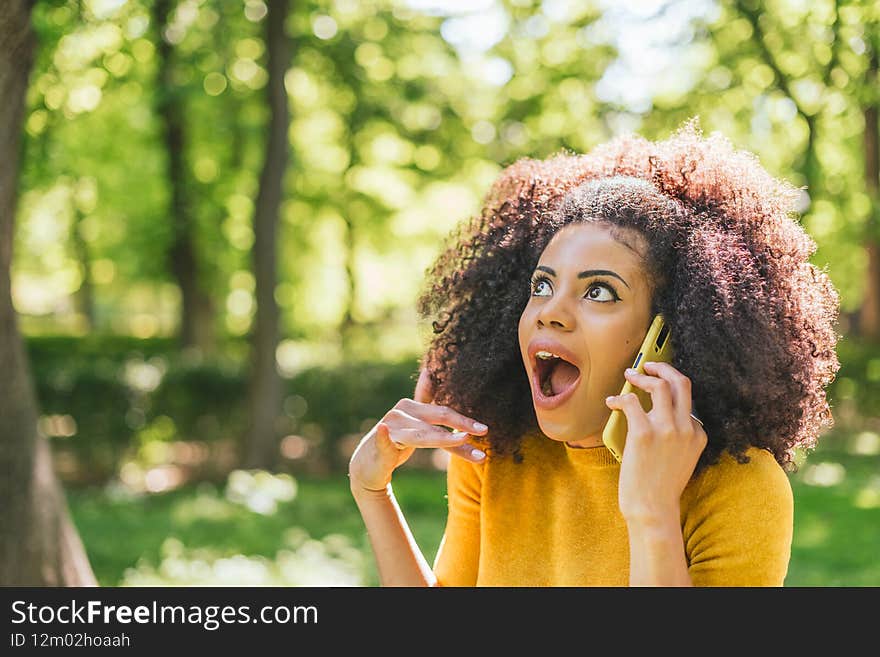 Pretty afro woman talking on the cellphone in amazement, in a garden.