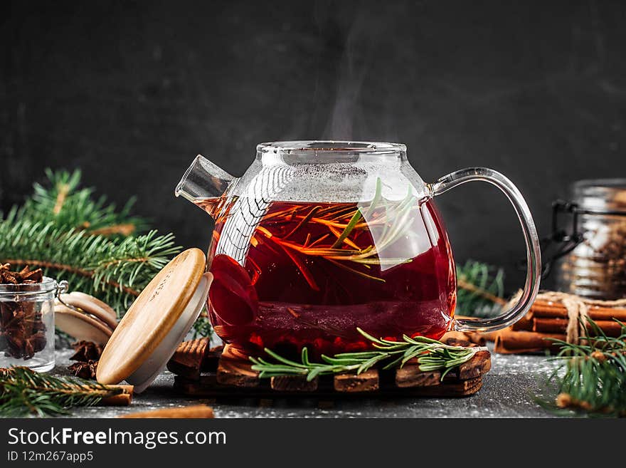 Glass kettle of fresh berry tea with rosemary on the decorated background