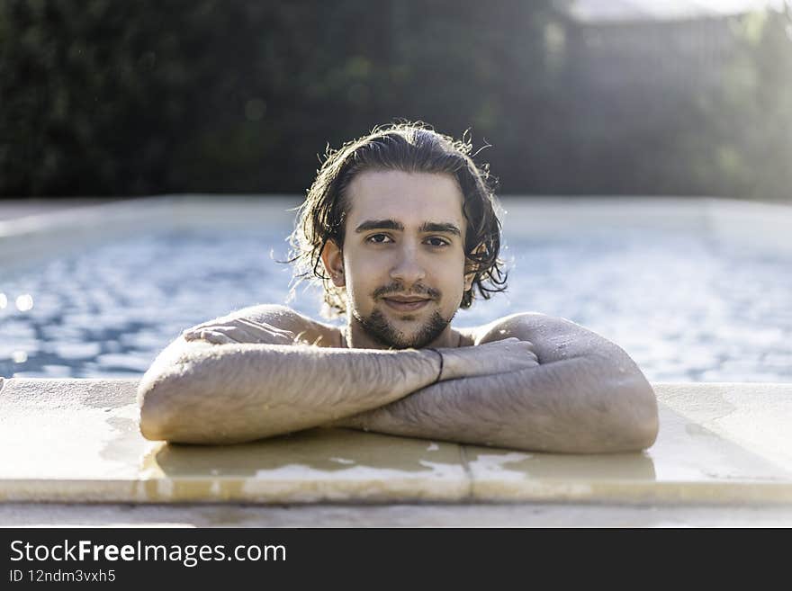 Young man leaning at the poolside with his arms crossed during summer vacation - Caucasian guy alone inside the swimming pool - Skincare and sunscreen concept