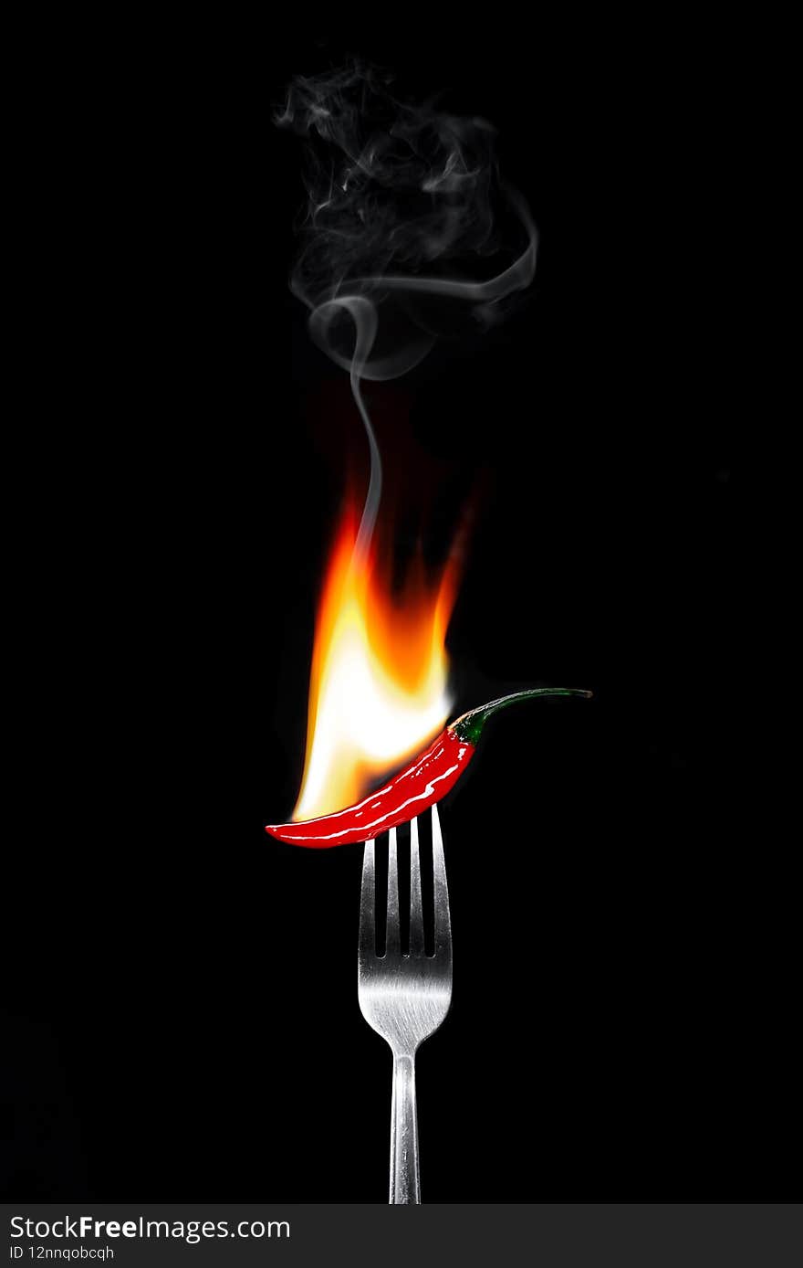 Hot red pepper with fire on a fork in black background