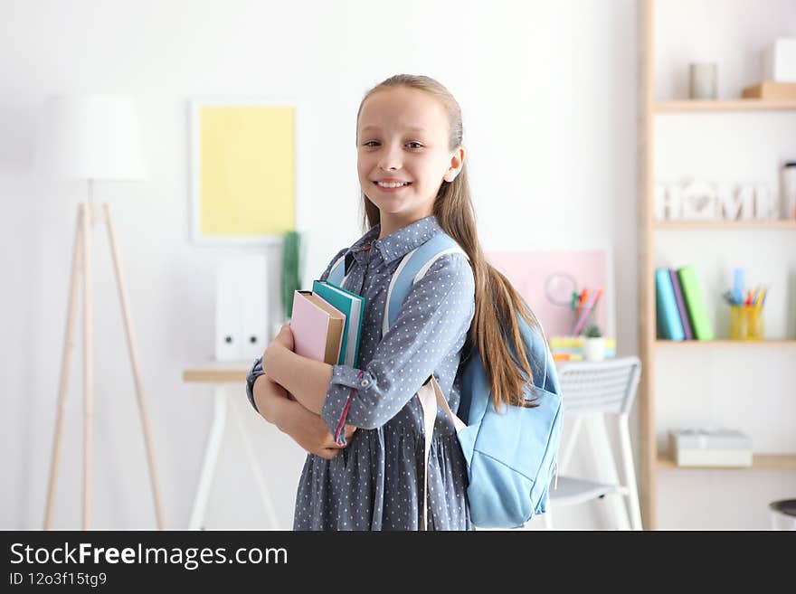 Cute cheerful schoolgirl puts stationery in a backpack. High quality photo