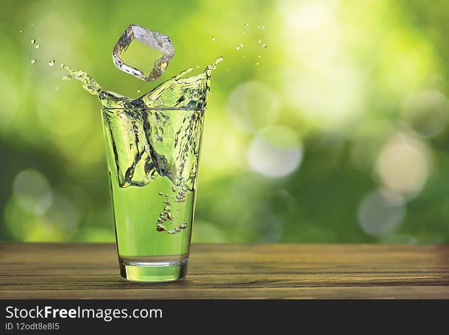 glass of water with splash and ice on wooden table outdoors. glass of water with splash and ice on wooden table outdoors