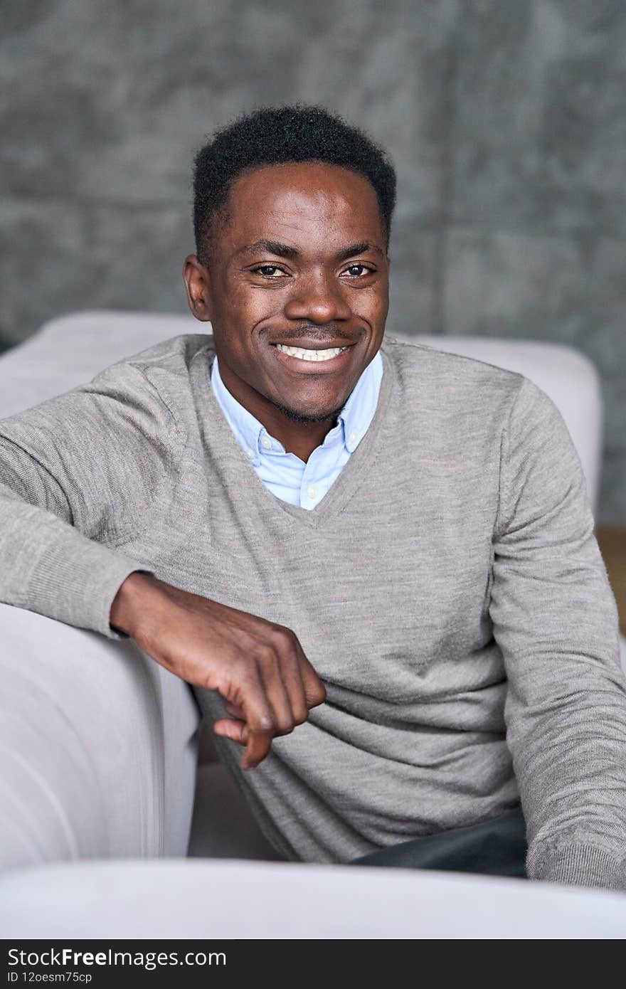 Young happy adult black man sitting on sofa at home looking at camera.