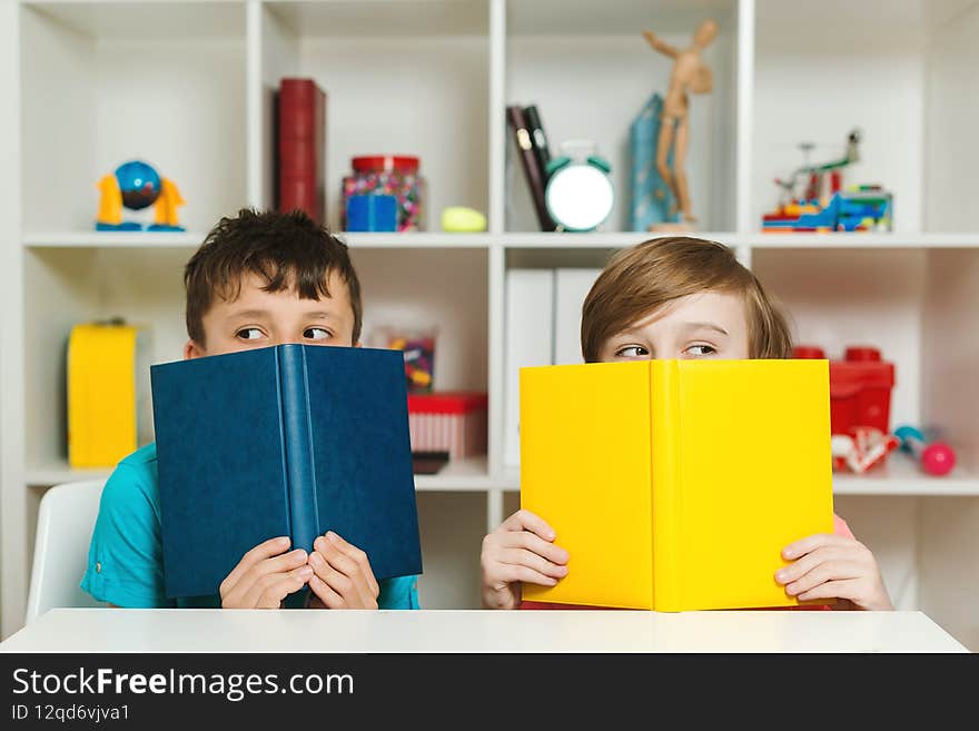 Two school boys hiding behind books at classroom. Happy friends having fun together after lesson. Education and development. Back to school concept. School children holding books