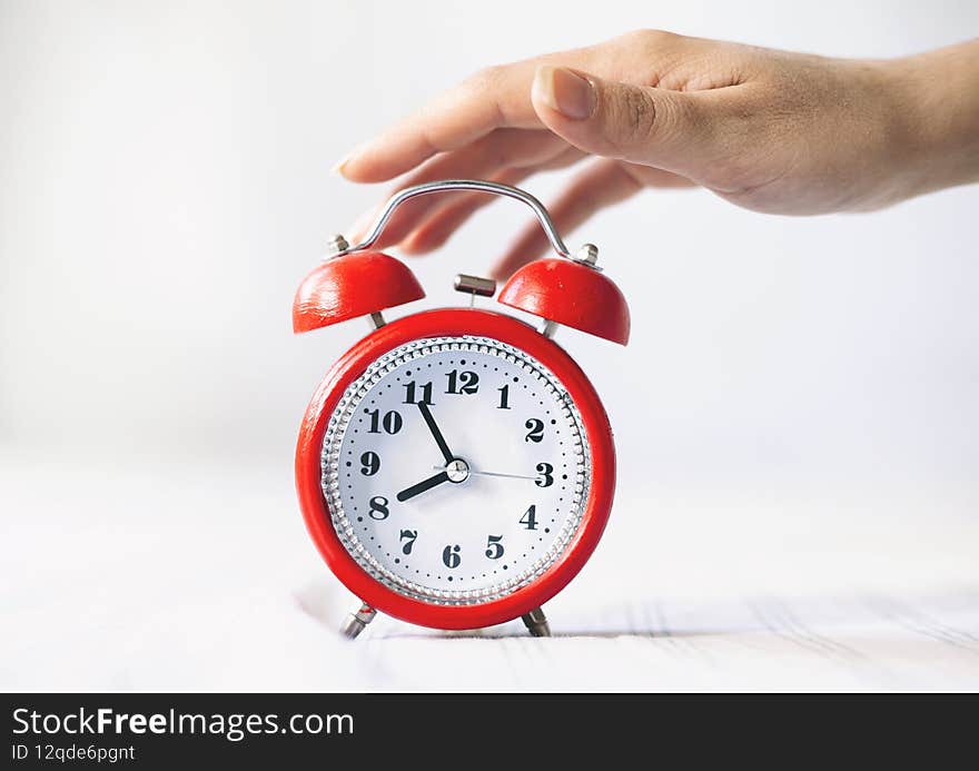 Time optimization concept. Female hand holding alarm clock on bed background, close up view